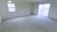 This single-floor space features a generously sized main living area finished with wall-to-wall plush carpeting in a neutral beige tone, creating a warm and inviting atmosphere. The room is bathed in natural light, courtesy of a double-pane window on the side wall and large sliding glass doors that lead to an outdoor balcony. The balcony, enclosed by a railing, offers views of the surrounding exterior environment, seamlessly connecting the interior to the outdoors. The walls are painted in a clean, neutral off-white tone, providing a versatile backdrop that complements a variety of interior design styles. The open layout of the living area allows for flexible furniture arrangement, making it well-suited for both relaxation and entertaining. The sliding glass doors not only enhance the brightness of the space but also provide convenient access to outdoor living. Overall, the space presents a bright, open, and functional environment with a clean, move-in-ready aesthetic.