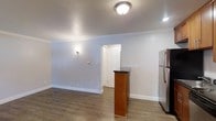This 2-bedroom, 1-bathroom single-floor residence delivers a clean, modern aesthetic through thoughtful finishes and an efficient layout. The open living and kitchen area is anchored by warm hardwood-style flooring that flows seamlessly throughout the space, creating a cohesive and inviting atmosphere. Crown molding frames the rooms with a polished architectural detail, while a textured ceiling adds subtle character overhead. The kitchen features a freestanding island with a dark countertop and warm wood cabinetry, providing both prep space and a natural dividing point between the kitchen and living areas. Stainless steel appliances, including a full-size refrigerator, complete the kitchen's functional appeal. Soft wall sconce lighting complements the overhead flush-mount fixtures, offering a warm and well-lit environment. Crisp white trim and baseboards contrast elegantly against the light gray walls, lending the space a fresh, contemporary feel. A six-panel interior door leads to additional areas of the home, maintaining a consistent and classic design language. The overall ambiance is bright, clean, and move-in ready, making this a practical and comfortable single-level home.