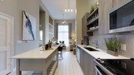 This well-appointed single-floor space showcases an open-concept layout that seamlessly connects the kitchen and living areas, creating a cohesive and functional flow throughout. The dramatic soaring ceilings immediately draw the eye upward, amplifying the sense of space and airiness, while a ceiling fan provides both style and comfort.

The kitchen is a standout feature, designed with modern wood-toned cabinetry, open shelving, and a tiled backsplash in neutral grey tones. A deep single-basin sink with a contemporary faucet anchors the countertop workspace, complemented by stainless steel appliances including a dishwasher and gas cooktop. A long central island with a crisp white countertop and bar seating serves as both a prep space and casual dining area, making it ideal for entertaining.

Pendant lighting with exposed bulbs adds an industrial-modern touch above the island, while light tile flooring runs throughout, reflecting natural light from the expansive floor-to-ceiling windows at the far end of the living area. The living space is warm and inviting, featuring a gallery wall, accent lighting, and soft drapery that frames the generous window. The overall ambiance is modern yet comfortable, with a neutral palette of warm greens, greys, and natural wood tones tying the entire space together.