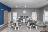Located at 3233 Campus Pointe Cir in Gainesville, Georgia, this single-floor space is thoughtfully designed to serve as a functional community hub. The interior is finished in a contemporary neutral gray palette, accented by a bold navy blue feature wall that adds depth and visual interest throughout.

The main lounge area offers a welcoming atmosphere, furnished with rich burgundy leather seating, round tables with metal chairs, and a plush area rug over wood-look flooring. Multiple windows dressed in white blinds and curtain panels flood the space with natural light. A coffee station provides a convenient amenity for visitors and residents alike.

Adjacent to the lounge, a dedicated meeting or study room is highlighted by the striking navy accent wall, on which a large whiteboard is mounted — ideal for collaborative work or presentations. A French glass door connects this room to the rest of the space, maintaining an open and connected feel while offering a degree of separation.

The built-in computer workstation area features a long, white cabinetry-style desk fitted with multiple monitors and printers, designed to accommodate several users simultaneously. Recessed lighting throughout ensures consistent, well-lit conditions across all areas. Together, these spaces create a balanced environment well-suited for studying, meetings, and community gatherings.