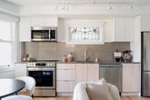 This contemporary townhouse in Vancouver offers 910 square feet of living space across three floors. The property boasts three bedrooms, including a spacious 150 square foot primary bedroom, and one bathroom. The interior is characterized by its bright and airy atmosphere, with white walls and light wood flooring throughout.

The home's design incorporates unique architectural elements, such as stained glass transoms above some windows, adding character and filtered natural light. Large windows in the living areas provide ample daylight and picturesque views of the surrounding neighborhood, including glimpses of autumn foliage.

The kitchen is a highlight, featuring modern white cabinetry, stainless steel appliances, and a stylish backsplash. Track lighting and under-cabinet illumination enhance the functional workspace. The open concept layout seamlessly connects the kitchen to the living area, ideal for entertaining.

The bathroom, while compact, is efficiently designed with a combination tub-shower, modern fixtures, and continuation of the light wood flooring. Storage solutions are integrated throughout the home, including built-in closets and shelving.

Multiple staircases connect the three floors, creating an interesting vertical flow within the townhouse. The property's location in Vancouver's vibrant Eastward H2 area (V5N 4L3) offers the perfect blend of urban convenience and residential charm, making it an attractive option for those seeking a contemporary living space in a dynamic city setting.