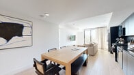 Located at 4971 S Centinela Ave in the Mar Vista neighborhood of Los Angeles, this single-floor unit offers a thoughtfully designed modern interior with a clean, minimalist aesthetic throughout. Light-toned wide-plank hardwood flooring extends across the entire space, creating a warm and cohesive feel.

The open-plan living, dining, and kitchen area serves as the heart of the unit. The kitchen features full-height dark cabinetry paired with stainless steel appliances, including a gas range, dishwasher, and over-range microwave, creating a striking contrast against the bright white walls. A large natural wood dining table with mixed seating anchors the dining area, while abstract wall art adds a curated artistic touch.

The living area is bathed in natural light from a floor-to-ceiling sliding glass door that opens to a private balcony, offering open views of the surrounding Los Angeles neighborhood, including palm trees and the city skyline. The living room is a comfortable, light-filled retreat with a wall-mounted flat-screen TV.

The bedroom continues the modern design language, featuring another set of sliding glass doors leading to the balcony, dark built-in wardrobes, and ample natural light. A second, more compact bedroom provides a versatile space with a wall-mounted desk. The bathroom is finished with large-format stone-look tiles and a sleek glass-enclosed walk-in shower with black fixtures and open wood shelving.