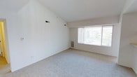This single-floor residence features two bedrooms and two bathrooms, offering a comfortable and functional layout well-suited for a range of lifestyles. The living area is notably open and airy, characterized by tall white walls that enhance the sense of volume and contribute to the space's bright, clean atmosphere. Soft neutral carpeting covers the floors, adding warmth underfoot while maintaining the understated color palette throughout.

A large window fitted with vertical blinds anchors the main living area, inviting generous natural light and providing outdoor views of surrounding greenery. The window's placement ensures the room feels well-lit throughout the day. Visible HVAC vents are integrated into the walls, ensuring climate comfort across the space.

The overall aesthetic is minimal and move-in ready, with white walls and light tones creating a versatile backdrop that adapts easily to a variety of furnishing styles. The single-floor layout adds to the ease of living, eliminating the need to navigate stairs. With two full bathrooms complementing the two bedrooms, the home offers practical convenience for residents or roommates alike.
