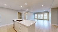 This well-appointed 3-bedroom, 2-bathroom residence at 49 Brookline Drive in Halifax, Nova Scotia offers a thoughtfully designed open-concept layout with a bright, contemporary aesthetic throughout. Light hardwood-style flooring flows seamlessly across the main living areas, complemented by soft neutral tones and recessed lighting that enhance the airy atmosphere.

The kitchen is a standout feature, showcasing crisp white cabinetry, a large central island with a white quartz countertop and undermount sink, subway tile backsplash, and a full suite of stainless steel appliances including a range, over-the-range microwave, refrigerator, and dishwasher. The kitchen opens directly into the spacious living area, which is fitted with a wall-mounted mini-split system for efficient climate control and large windows that draw in natural light.

The generously sized primary bedroom offers a bright window with outdoor views, while the additional bedrooms maintain the same clean, neutral finishes. Both bathrooms are finished with tile flooring and include a tub-shower combination with crisp white tile surround. A dedicated laundry area houses a full-size washer and dryer alongside built-in shelving for added storage convenience. The private balcony features glass-panel railings and overlooks a natural, wooded landscape.
