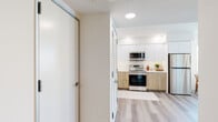 Located at 3170 W Olympic Blvd in Los Angeles, this thoughtfully designed single-floor residence blends modern aesthetics with everyday functionality. The open layout is anchored by light-toned hardwood-style flooring that flows seamlessly throughout, creating a cohesive and airy feel.

The kitchen is a standout feature, showcasing a two-tone design with crisp white upper cabinetry and warm wood-grain lower cabinets, complemented by a classic white subway tile backsplash, quartz countertops, and stainless steel appliances including an electric range and over-the-range microwave.

The living area is bright and inviting, benefiting from large windows that frame views of the surrounding Los Angeles cityscape and provide generous natural light. Recessed lighting throughout further enhances the clean, contemporary atmosphere.

The bedroom offers a calm retreat, distinguished by a slate-blue accent wall, plush carpeting, and a mirrored sliding closet that amplifies the sense of space. Natural light filters in through wide, slatted shade windows.

The bathroom is finished to a high standard, featuring large-format gray tile surrounding a soaking tub, wood-accented cabinetry with built-in shelving, a wide vanity mirror, and durable wood-look flooring — striking a balance between style and practicality throughout.