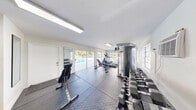 Located at 3600 Jackson St in Hollywood, Florida, this fitness center offers a single, well-appointed exercise room designed to support a comprehensive workout routine. The space features durable rubber interlocking floor mats covering the main workout area, complemented by tile flooring near the entrance, providing both functionality and easy maintenance.

The room is equipped with a variety of exercise equipment, including an elliptical machine, a cable weight machine, adjustable workout benches, and a multi-tiered dumbbell rack stocked with a range of hex weights. A full-length wall mirror allows users to monitor their form during exercise. Fitness reference charts are posted on the walls for guidance.

Natural light floods the space through large sliding glass doors and windows that line one wall, offering direct views of a sparkling outdoor pool surrounded by tropical palm trees — creating an energizing, resort-like atmosphere. A wall-mounted air conditioning unit ensures year-round comfort. Overhead fluorescent lighting and a skylight further brighten the interior.

The bright white walls and clean layout give the fitness center an open, airy feel. The sliding glass doors provide convenient direct access to the pool area, seamlessly connecting indoor fitness with outdoor recreation in this sunny South Florida setting.