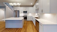 Located at 111 Locust St in Woburn, MA, this three-floor home offers a thoughtfully designed layout with contemporary finishes throughout. The main living area features warm hardwood flooring, soft neutral wall tones, recessed lighting, and large windows that allow ample natural light to fill the space. A door provides convenient access to the outdoors, enhancing the open, airy feel of the room.

The kitchen is a standout feature, showcasing white shaker-style cabinetry extending to the ceiling, light quartz countertops, a subway tile backsplash, and a central island. Stainless steel appliances—including a refrigerator, range, built-in microwave, and dishwasher—complete this functional and elegant space. Pendant lighting and hardwood floors add warmth and character.

The bathrooms are finished with white vanities, marble-style countertops, brushed gold or nickel hardware, and clean tile flooring. One bathroom includes accessibility grab bars, reflecting thoughtful, inclusive design. A bright half-bath with a window-mounted vanity offers additional convenience.

Upper-level bedrooms are carpeted and bathed in natural light from multiple windows with neighborhood views. Generous walk-in closet space with wire shelving provides ample storage.

The unfinished basement level offers substantial open space with visible mechanicals and utility infrastructure, presenting excellent potential for future customization or storage use.