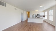This single-floor residence offers a thoughtfully designed open-concept layout that seamlessly connects the living area and kitchen. The main living space features warm hardwood-style flooring and an abundance of natural light, courtesy of multiple large windows that offer views of the surrounding greenery. A glass-paneled door provides additional light and exterior access from the living area.

The kitchen is a standout feature, equipped with stainless steel appliances including a refrigerator, range, and over-the-range microwave. Crisp white cabinetry pairs elegantly with granite countertops and a gray subway tile backsplash. A generously sized kitchen island with a built-in sink and granite surface serves as both a functional workspace and a natural gathering point.

The bedrooms are carpeted for comfort and feature ample closet space. One bedroom includes a walk-in closet and direct access to a private en suite bathroom fitted with a vanity, walk-in shower, and a separate water closet. A second full bathroom offers a combination tub and shower, tile flooring, and a clean white vanity. The overall design palette of neutral tones and clean lines creates a bright, welcoming ambiance throughout the residence.