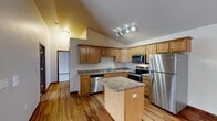 This single-floor residence offers a thoughtfully designed layout that balances comfort and functionality throughout. The kitchen serves as a central highlight, featuring warm honey-toned cabinetry, granite-style countertops, a full suite of stainless steel appliances including a refrigerator, electric range, microwave, and dishwasher, and a central island that provides additional prep space. Light hardwood flooring runs through the kitchen and connects seamlessly to adjoining areas. Vaulted ceilings lend an open, airy quality to the living spaces, with the main living area benefiting from a sliding glass door that opens to a private balcony overlooking the surrounding area. The bedrooms are finished with plush carpeting and feature rich, dark-stained wood doors, with the primary bedroom offering generous closet space complete with built-in shelving and hanging rods. A dedicated walk-in storage closet adds further practicality. The bathroom is well-appointed with a wood-accented vanity, granite-style countertop, and a clean walk-in shower. A full-size washer and dryer are conveniently housed within the unit. Baseboard heating is present throughout, and ceiling fans in the bedrooms contribute to year-round comfort.
