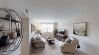 Located at Olde Hill Court in Columbus, Ohio, this single-floor unit offers a well-organized and comfortable layout designed for everyday living. The living room serves as the heart of the home, featuring soft carpeting, neutral walls, and natural light streaming through large windows with curtains. The open sightlines connect the living area to the entryway, creating a sense of flow and spaciousness throughout. A dedicated dining area sits adjacent to the kitchen, which is equipped with warm wood cabinetry, light vinyl plank flooring, a full suite of black appliances including a refrigerator, electric range, and over-the-range microwave, along with ample counter space and a sink beneath upper cabinets. The unit includes two bedrooms, each carpeted and featuring windows that bring in natural light. The primary bedroom offers generous proportions and a calm, neutral palette, while the second bedroom is equally comfortable with its own window and soft tones. The full bathroom is finished with light wood-look flooring, a combined tub and shower, a single-sink vanity with cabinet storage below, and a mirrored medicine cabinet above. The overall design of the unit is practical and inviting, providing a cohesive and livable environment throughout.