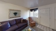 This single-floor residence offers a thoughtfully organized layout designed for comfortable everyday living. The living room serves as a welcoming gathering space, featuring carpet flooring, a large front-facing window with window treatments that allow natural light to filter in, and a front entry door. The room accommodates a sofa, recliner chair, and a glass coffee table, with a decorative framed mirror adding visual depth to the neutral-toned walls.

The kitchen is well-equipped with light wood cabinetry, dark laminate countertops, and a full suite of black appliances including a range, over-the-range microwave, refrigerator, and dishwasher. A double-basin sink is positioned along the peninsula, which also provides a convenient breakfast bar that opens toward the dining area. Tile flooring runs throughout the kitchen for easy maintenance.

Adjacent to the kitchen, a dedicated laundry closet houses a full-size washer and dryer, adding a practical in-unit convenience. The bedroom is generously sized with plush carpet flooring and features a sliding glass door that opens to an outdoor area, allowing natural light and exterior views to enhance the room's airy feel. The bathroom includes a tub and shower combination enclosed by sliding frosted glass doors, a toilet, and a vanity with dark countertop surfaces and tile flooring.