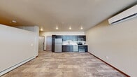 This thoughtfully designed 1-bedroom, 1-bathroom unit offers a functional and modern living experience across a single floor. The open-concept layout seamlessly connects the kitchen and living area, creating a bright, airy atmosphere enhanced by recessed lighting and wood-look flooring that flows throughout the entire unit. The kitchen is a standout feature, equipped with a full suite of stainless steel appliances — including a refrigerator, electric range, microwave, and dishwasher — complemented by two-toned cabinetry in dark blue-gray and espresso tones, white countertops, and a classic subway tile backsplash. The living area benefits from natural light streaming through clerestory windows flanking the front entry door, adding a sense of openness. The bedroom is a cozy, well-proportioned retreat equipped with a ceiling fan. Directly accessible from the bedroom corridor is a full bathroom featuring a white vanity with a vessel sink and light-toned countertop, alongside a walk-in closet outfitted with built-in shelving and hanging rods for ample storage. A dedicated in-unit laundry area with a stacked washer and dryer adds convenience. Baseboard heating is present throughout, and neutral warm-beige walls create a clean, move-in-ready aesthetic.