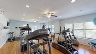 The fitness center at 209 New Chalet Dr in Mohegan Lake, NY is a well-appointed, single-floor facility designed to support a comprehensive workout experience. The space features warm hardwood flooring throughout, accented by white wainscoting along the walls and soft blue-gray paint, creating a clean and inviting atmosphere. Recessed lighting and ceiling fans with light fixtures ensure the room remains bright and comfortable during any session.

The cardio zone is generously equipped with multiple Landice treadmills, elliptical trainers, and a stair climber, as well as a recumbent bike and upright cycle. Rubber floor mats are placed beneath each machine for safety and protection. The strength and free weight area includes a dumbbell rack with a full range of weights, an adjustable workout bench, a multi-function cable machine, and a leg press, supported by posted exercise reference charts on the wall. Stability balls add versatility for core training.

Multiple windows along the perimeter flood the space with natural light and provide outdoor views, enhancing the overall workout environment. Wall-mounted flat-screen TVs and a water cooler add convenience for users. A dedicated restroom is accessible directly from the fitness floor. The layout is thoughtfully organized to allow ample space for movement between equipment zones.