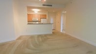 This single-floor residence presents a well-planned open-concept layout that seamlessly connects the kitchen and living areas. The kitchen is equipped with light wood cabinetry, white appliances including a built-in microwave and refrigerator, and a dark granite-topped breakfast bar that serves as both a workspace and a casual dining surface. Recessed lighting and a ceiling-mounted light fixture provide ample illumination throughout the kitchen area.

The living space extends generously from the kitchen, featuring neutral-toned wall-to-wall carpeting that lends a warm and comfortable feel underfoot. Recessed ceiling lights and a centrally located HVAC vent contribute to a practical and comfortable environment. The clean, white walls and simple trim work give the space a bright and airy ambiance.

A hallway visible from the main living area leads to additional rooms, suggesting a thoughtful floor plan designed for ease of movement throughout the home. The overall aesthetic is clean, neutral, and move-in ready, making it a versatile space suitable for a variety of furnishing styles. The open layout allows for flexible furniture arrangements, maximizing the functional potential of the living area.