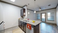 Located at 4651 S Custer Rd in McKinney, TX, this well-appointed 1-bedroom, 1-bathroom unit offers a thoughtfully designed single-floor layout. The open-concept kitchen and living area serves as the heart of the home, featuring a central island with granite countertops, a stainless steel sink, and pendant lighting overhead. Dark espresso cabinetry with subway tile backsplash contrasts beautifully against the light wood-style flooring, while stainless steel appliances — including a refrigerator, range, microwave, and dishwasher — complete the kitchen. A ceiling fan overhead and a glass door leading to the private patio fill the living area with natural light. The bedroom offers cozy carpeting, a ceiling fan, and a generous window. Three closets provide ample storage throughout the unit. The bathroom includes a granite-topped vanity with dark cabinetry, wood-style tile flooring, and a tub/shower combination with subway tile surround, accompanied by a walk-in closet. Additional conveniences include a dedicated laundry area and utility room. Crown molding accents the walls throughout, adding a polished finishing touch to this efficiently designed space.