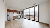 This modern one-bedroom, one-bathroom unit is designed with clean lines and contemporary finishes, offering an efficient and well-appointed living space. The open-concept main area is anchored by dramatic floor-to-ceiling windows that frame sweeping city skyline views, flooding the interior with natural light and creating a striking urban backdrop. Light-toned tile flooring runs throughout, complementing the bright white walls and creating a cohesive, airy aesthetic. A structural concrete column adds an industrial design element to the living area.

The kitchen is thoughtfully outfitted with rich dark wood cabinetry, a classic white subway tile backsplash, and a full suite of stainless steel appliances, including a side-by-side refrigerator, range, microwave, and dishwasher. Light countertops provide ample workspace, making the kitchen as functional as it is stylish.

The bedroom is a comfortable retreat, featuring wood-look flooring and access to a dedicated walk-in closet with built-in shelving and hanging space. The bathroom is finished with white subway tile walls, a sliding glass-enclosed walk-in shower, mosaic tile flooring, and clean chrome fixtures, delivering a polished and timeless look. Recessed lighting throughout the unit adds to the modern, refined ambiance of this well-designed urban residence.