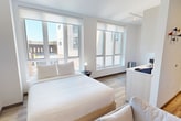 Located on the third floor at 212 S 4th Ave in Ann Arbor, Michigan, this 390-square-foot studio apartment offers a clean, modern aesthetic throughout its efficiently designed single-floor layout. The living area features light wood-look flooring, crisp white walls, and a wall-mounted flat-screen TV, creating a bright and functional space ideal for everyday living. Large windows flood the sleeping area with abundant natural light while providing open views of the surrounding Ann Arbor cityscape, enhancing the sense of space despite the compact footprint. The galley-style kitchen is equipped with stainless steel appliances — including a refrigerator, range, and over-the-range microwave — complemented by white cabinetry, a stainless steel sink with a flexible-head faucet, and light wood flooring that carries throughout the unit. The bathroom showcases a sleek, contemporary design highlighted by a backlit vanity mirror, a white quartz countertop, white cabinetry, and marble-style tile flooring, delivering a polished, spa-like atmosphere. A walk-in closet visible from the bathroom provides practical storage solutions. The unit's consistent use of neutral tones, modern fixtures, and quality finishes creates a cohesive, sophisticated living environment well-suited for urban Ann Arbor living.
