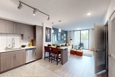 Located in Coral Springs, FL, this well-appointed 2-bedroom, 1-bathroom residence offers a thoughtfully designed open-concept layout finished with light wood-style flooring throughout. The modern kitchen is equipped with stainless steel appliances, including a French door refrigerator, range, microwave, and dishwasher, complemented by sleek wood-grain cabinetry, white subway tile backsplash, and light countertops. A kitchen island with bar seating creates a seamless transition into the dining and living areas. The living room features a bold teal accent wall, track and pendant lighting, and floor-to-ceiling sliding glass doors that flood the space with natural light and open to a private balcony with outdoor seating. The spacious primary bedroom also enjoys direct balcony access through large sliding glass doors framing lush greenery views, while a walk-in closet provides generous storage. The full bathroom is finished with marble-style tile surrounding a soaking tub, tile flooring, a white vanity, and a large mirror. A dedicated closet area adjacent to the bathroom adds additional storage convenience. The overall ambiance is contemporary and bright, with clean lines and modern detailing throughout.
