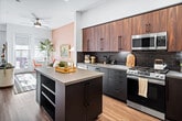 Located at 2590 Red Hill Avenue in Santa Ana, CA, this single-story residence offers a thoughtfully designed layout encompassing one bedroom, one bathroom, and a fully equipped kitchen. The kitchen is a standout feature, showcasing rich walnut upper cabinetry, dark lower cabinets with matte black hardware, and a bold black subway tile backsplash. A central island with a grey quartz countertop provides additional prep space, while stainless steel appliances — including a gas range, built-in microwave, dishwasher, and refrigerator — complete the functional and contemporary design. Hardwood-style flooring flows throughout, connecting the kitchen to the open living area, which benefits from multiple windows and a glass door leading to a private outdoor space, filling the room with natural light. The generously sized primary bedroom features high ceilings, a pendant light fixture, and ample room for furnishings. The bathroom offers distinctive hexagonal floor tile, an intricately patterned accent wall, and a clean, modern aesthetic. This residence combines practical functionality with carefully curated design details, making it a comfortable and visually engaging living space.