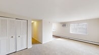 Located at 18 N Oak Ave in Clifton Heights, Pennsylvania, this single-floor unit offers a clean, neutral aesthetic throughout. The living area is generously sized, finished with wall-to-wall carpeting and bright white walls that create an open, airy feel. Multiple windows allow natural light to filter in, complemented by baseboard heating and a wall-mounted air conditioning unit for year-round comfort. The layout flows from the main living space into additional rooms, each carpeted and featuring louvered bi-fold closet doors that provide ample storage. The kitchen is outfitted with warm honey-toned oak cabinetry, offering plentiful upper and lower storage, a stainless steel sink, light countertops, and a white electric range with overhead ventilation. The flooring in the kitchen transitions to hardwood-style planking, providing a practical and easy-to-maintain surface. The bathroom features tile flooring, a white vanity with storage, a toilet, and a shower/tub combination, all finished in a neutral palette that keeps the space feeling clean and functional. Throughout the unit, the consistent use of white trim, neutral tones, and practical finishes creates a cohesive and move-in-ready environment suited for comfortable everyday living.