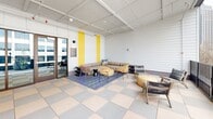 Located in the heart of uptown Charlotte at 426 N Tryon St, this single-floor lounge space offers a vibrant and well-appointed communal living area that seamlessly blends indoor comfort with outdoor accessibility. The interior is defined by crisp white shiplap walls accented with bold yellow vertical panels, creating a bright and energetic ambiance. A coffered ceiling with an open grid design adds architectural interest and a sense of height to the space.

The living area is furnished with a large, tufted sectional sofa anchored by a patterned blue area rug, complemented by an eclectic mix of rattan chairs, lounge chairs, and woven pouf ottomans that encourage relaxed, social gatherings. A wall-mounted flat-screen television serves as a central focal point along the main wall. The distinctive large-format checkered tile flooring in muted tones of gray, cream, and blue lends a playful yet sophisticated character throughout.

Floor-to-ceiling glass doors open directly onto a wraparound balcony, where additional seating takes full advantage of sweeping views of Charlotte's urban skyline. The balcony is framed by sleek black metal railings, offering an elevated vantage point over the surrounding cityscape. Natural light floods the interior through the expansive glass wall, creating a bright and welcoming atmosphere throughout the day.