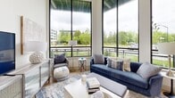 Located at 2031 Maywill St in Richmond, Virginia, this single-floor residence showcases a thoughtfully designed contemporary interior with high ceilings and abundant natural light throughout. The living area is a standout, featuring dramatic floor-to-ceiling windows with sleek black frames that frame lush green outdoor views and provide a seamless connection to the surrounding landscape. A private balcony extends the living space outdoors. The kitchen is a functional and visually striking space, appointed with bold slate-blue cabinetry, white quartz countertops, stainless steel appliances, and light hardwood flooring — a combination that is both practical and aesthetically cohesive. Multiple bedrooms offer a calm, restful atmosphere, each with generous windows, light neutral walls, and warm wood flooring. Soaring ceiling heights in the bedroom areas enhance the sense of openness and airiness. The bathrooms are well-appointed with light tile flooring, white vanities featuring modern hardware, large mirrors, and ample counter space. The primary bath includes a glass-enclosed walk-in shower, while the secondary bath offers a full tub-shower combination. Throughout the residence, a consistent palette of soft neutrals, natural wood tones, and blue accents creates a cohesive and inviting ambiance.