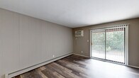 Located at 1800 Park West Blvd in Griffith, Indiana, this two-bedroom, two-bathroom residence offers a practical and well-organized single-floor layout. The combined living and dining area serves as the heart of the home, featuring rich wood-style plank flooring, neutral taupe walls, a ceiling fan, and a sliding glass door that floods the space with natural light and provides views of surrounding greenery. Baseboard heating and a wall-mounted A/C unit ensure year-round comfort throughout the living areas.

The galley-style kitchen is outfitted with bold dark cabinetry, white countertops, a stainless steel sink, and black appliances including a range and refrigerator, creating a striking contrast that adds visual interest to the functional space. Wood-style flooring continues throughout the kitchen for a cohesive look.

Both bedrooms feature plush neutral carpeting, individual windows with blinds for natural light and privacy, and wall-mounted A/C units with baseboard heating. The primary bedroom offers a comfortable, well-proportioned retreat.

The two bathrooms are finished with clean white square tile surrounds and full tub-shower combinations, maintaining a bright and functional aesthetic. A dedicated closet adds practical storage to complete this straightforward and comfortable residence.
