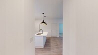 Located at 7243 US-431 N in Owens Cross Roads, Alabama, this single-story residence showcases a clean, modern aesthetic with thoughtful finishes throughout. The open-concept kitchen serves as the heart of the home, centered around a large white island with a matte black faucet and undermount sink, illuminated by a pair of bold black pendant lights. Upper white shaker cabinets contrast beautifully with light wood lower cabinetry, complemented by a marble-look tile backsplash, quartz countertops, stainless steel appliances, and a convenient walk-in pantry with built-in shelving. Light luxury vinyl plank flooring flows seamlessly through the main living areas, while a glass door and large window invite abundant natural light into the open living space. The bedrooms feature soft wall-to-wall carpeting and ceiling fans, with windows providing natural light and a bright, airy feel. The primary bathroom is a well-appointed retreat, offering a dual-sink floating vanity in light wood tones, matte black fixtures, a large framed mirror, and a glass-enclosed marble-tiled shower, along with a dedicated walk-in closet featuring multi-tiered shelving. The overall design balances contemporary style with functional comfort throughout.