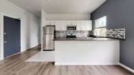 Located at 1423 Magnolia Ave in Los Angeles, Unit 204 is a thoughtfully designed single-floor residence that blends modern finishes with functional living. The open-concept kitchen serves as a centerpiece of the home, featuring crisp white shaker cabinetry extending to the ceiling for ample storage, dark charcoal countertops, and a mosaic tile backsplash in neutral tones. A full suite of stainless steel appliances — including a refrigerator, gas range, built-in microwave, and dishwasher — completes the space. Light tile flooring in the kitchen transitions smoothly into warm wood-style laminate flooring that carries throughout the main living areas, creating a cohesive and inviting atmosphere. The bedroom is generously proportioned, finished with the same light laminate flooring, bright white walls, and a ceiling fan with light fixture overhead. A sliding-door closet provides practical storage. The bathroom showcases a clean, minimalist design with light linear tile flooring, white fixtures, a vanity with under-sink cabinet, a wall-mounted mirror cabinet, and a marble-accented shower surround. A window in the bathroom allows natural light to filter in with views of surrounding greenery, enhancing the bright and airy feel throughout this well-appointed Los Angeles residence.