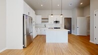 Located at 7831 E Union Ave in Denver, Colorado, this thoughtfully designed one-bedroom, one-bathroom residence offers a clean, modern aesthetic throughout its efficiently utilized single floor. The open-concept kitchen serves as the heart of the home, showcasing white shaker cabinetry, a classic subway tile backsplash, sleek light-colored countertops, and a full suite of stainless steel appliances including a refrigerator, range, and built-in microwave. A central island with pendant globe lighting above adds both functional prep space and a stylish focal point, while warm-toned hardwood-style flooring runs throughout the main living areas. The bedroom is a calm, light-filled retreat featuring plush carpeting, tall ceilings, and large windows that frame views of the Denver skyline, allowing abundant natural light to pour in. A dedicated closet provides organized storage. The full bathroom continues the modern design language with a white vanity, large framed mirror, and a tub-shower combo adorned with marble-look tile surround. Additional conveniences include an in-unit laundry area and a utility room. The overall ambiance is bright, clean, and contemporary, making for a polished urban living experience.
