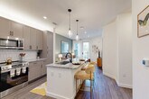 Located at 515 Royal Court in Charlotte, NC, this well-designed one-bedroom, one-bathroom residence offers a thoughtful single-floor layout with modern finishes throughout. The open-concept kitchen and living area serves as the heart of the home, featuring a large granite-topped island with seating for two, taupe shaker-style cabinetry, a white subway tile backsplash, and stainless steel appliances including a French door refrigerator. Pendant lighting over the island adds a refined touch. The living room flows seamlessly from the kitchen and is bathed in natural light from a glass door leading to a balcony with city views. A sage green accent wall adds warmth and character to the space. Wood-style plank flooring runs throughout the entire residence, providing a cohesive and contemporary aesthetic. The spacious primary bedroom features a window with natural light, a dedicated closet, and a clean, neutral palette. The bathroom is appointed with granite countertops, taupe cabinetry with matte black hardware, a large framed mirror, and built-in open shelving for added storage. Recessed lighting throughout and crisp white walls contribute to a bright, airy ambiance that makes this Charlotte residence feel polished and inviting.