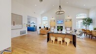 Located at 4630 S Lakeshore Dr in Tempe, Arizona, this single-floor space offers a generously sized, open-concept layout that seamlessly blends the living and dining areas into one cohesive, welcoming environment. The architecture is defined by dramatically high vaulted ceilings that amplify the sense of openness, while a series of arched windows flood the interior with abundant natural light and provide views of the surrounding outdoor greenery.

The flooring transitions elegantly between warm-toned hardwood and light-colored tile, delineating functional zones while maintaining a unified aesthetic. Structural archways and white-painted columns frame the interior, adding architectural character throughout. The living area centers around a tiled fireplace flanked by built-in shelving, complemented by a stylish chandelier overhead. Large arched windows positioned high on the walls draw the eye upward and enhance the airy atmosphere.

The dining zone features a long communal table with ample seating, accompanied by a bold navy-blue built-in counter area equipped as a workspace. Arched exterior doors and floor-to-ceiling windows at the entry invite natural light deep into the space. Colorful geometric tile accents at the base of columns add a vibrant, modern touch. The overall ambiance is bright, clean, and contemporary, making it a functional and visually appealing gathering space.