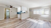 Located at 10767 Lawler St in the Palms neighborhood of Los Angeles, this single-story unit showcases a thoughtfully updated interior with a cohesive, contemporary design throughout. The open-concept living area features light wood-tone laminate flooring, crown molding, and a ceiling fan, creating a bright and airy atmosphere. Natural light filters in through plantation-shuttered windows, complementing the neutral gray and beige color palette. A wall-unit air conditioner provides climate control, and the kitchen is accessible directly from the living space via a half-wall pass-through.

The galley-style kitchen is well-appointed with white shaker cabinetry, dark quartz countertops, a blue tile backsplash, and stainless steel appliances including a gas range and refrigerator. A second room features the same laminate flooring and crown molding, offering versatility as a dining area or additional living space.

The bedrooms are carpeted and include crown molding, ceiling fans, and plantation shutters. One bedroom features a full-width mirrored sliding closet, adding depth and storage. The bathroom is cleanly renovated with a white vanity, dark quartz countertop, wood-look tile flooring, and a tub-shower combination enclosed by sleek black-framed glass sliding doors.