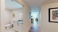 Located on the sixth floor at 2160 Van Buren Street in Hollywood, Florida, this apartment delivers a clean, contemporary aesthetic throughout its single-level layout. Light wood flooring runs continuously through the main living areas, complementing the neutral color palette and creating a cohesive, airy atmosphere.

The living area is a standout feature, anchored by expansive floor-to-ceiling sliding glass doors that open to a private balcony overlooking the surrounding cityscape and a pool below. Exposed concrete ceilings add an industrial design element that contrasts attractively with the otherwise polished interior.

The kitchen is well-appointed with white flat-panel cabinetry extending to the ceiling, granite countertops, stainless steel appliances including a refrigerator, range, and built-in microwave, and a deep undermount sink. Track lighting overhead ensures thorough illumination throughout the workspace.

The bedroom benefits from the same generous window treatment as the living area, with floor-to-ceiling glass framing outdoor views and allowing abundant natural light. A decorative ceiling treatment adds visual interest to the room.

Two bathrooms serve the unit. One features a granite-topped vanity, backlit mirror, and a glass-enclosed walk-in shower finished in large-format tile. The second bathroom includes a granite vanity and a tub-shower combination with textured tile surround and light porcelain flooring.