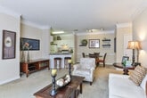 Located at 3920 Club Dr in Duluth, Georgia, this single-floor residence offers a thoughtfully designed layout that balances comfort and functionality. The entryway opens to a spacious living room finished with plush carpeting, crown molding, and generous natural light streaming through large windows dressed with decorative curtains. The living area flows seamlessly into a dedicated dining space, which features wall-mounted shelving and a glass-top dining table — ideal for everyday meals or entertaining guests. A breakfast bar with bar stools connects the dining area to the kitchen, which is outfitted with white cabinetry, dark countertops, a double sink, dishwasher, and full-size refrigerator, all set atop warm hardwood flooring. The primary bedroom is a serene retreat with carpeted floors, a walk-in closet, and an en suite bathroom featuring tile flooring, a single vanity, and a shower-tub combination. The second bedroom is equally comfortable, offering carpeted floors, a large window, and convenient access to a second full bathroom with a similar layout. Warm, neutral tones and crown molding details throughout give this residence a cohesive and welcoming ambiance.