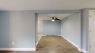 This single-floor residence offers a clean, modern aesthetic throughout, anchored by consistent light hardwood-style flooring and a cohesive cool blue-grey palette on the walls. The open living and dining areas are defined by a structural archway, creating a sense of distinction between spaces while maintaining an open flow. Ceiling fans with integrated lighting are present in multiple rooms, complementing the baseboard heating system found throughout. The bedrooms are well-proportioned, each featuring ceiling fans, natural light from windows with blinds, and baseboard heaters for year-round comfort. The kitchen is a standout feature, showcasing dark espresso-toned cabinetry, marble-look countertops, a mosaic glass tile backsplash in soft blue and grey tones, and black appliances including a range and refrigerator. A window above the sink brings in natural light. One living area opens directly to an outdoor patio through a sliding glass door, offering a seamless indoor-outdoor connection. The bathroom is clean and functional, featuring a full tub-shower combination with white tile surround and chrome fixtures. Crisp white trim and baseboards complete the refined, move-in-ready interior throughout.