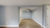 This single-floor residence offers a clean, modern aesthetic throughout, anchored by consistent light hardwood-style flooring and a cohesive cool blue-grey palette on the walls. The open living and dining areas are defined by a structural archway, creating a sense of distinction between spaces while maintaining an open flow. Ceiling fans with integrated lighting are present in multiple rooms, complementing the baseboard heating system found throughout. The bedrooms are well-proportioned, each featuring ceiling fans, natural light from windows with blinds, and baseboard heaters for year-round comfort. The kitchen is a standout feature, showcasing dark espresso-toned cabinetry, marble-look countertops, a mosaic glass tile backsplash in soft blue and grey tones, and black appliances including a range and refrigerator. A window above the sink brings in natural light. One living area opens directly to an outdoor patio through a sliding glass door, offering a seamless indoor-outdoor connection. The bathroom is clean and functional, featuring a full tub-shower combination with white tile surround and chrome fixtures. Crisp white trim and baseboards complete the refined, move-in-ready interior throughout.