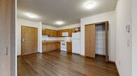 This single-floor residential unit offers a practical and well-organized layout designed for comfortable everyday living. The kitchen serves as a functional centerpiece, featuring warm honey-toned oak cabinetry that extends from base to upper wall, providing generous storage throughout. White appliances include a coil-top electric range, over-the-range microwave, and a full-size refrigerator. A built-in pantry with open wire shelving adds additional storage capacity. The kitchen flows naturally into the main living area, which is finished with durable hardwood-style flooring and benefits from natural light streaming through multiple windows fitted with horizontal blinds. Baseboard heating runs throughout the unit, ensuring consistent warmth. The bedrooms offer a mix of hardwood-style and plush carpeted flooring, each with windows that provide outdoor views and natural light. The bathroom features earthy ceramic tile flooring, a single-sink vanity with oak cabinetry, a large mirror, and a shower-tub combination. A textured ceiling is present in the kitchen and select areas, while the living and sleeping spaces feature smooth, neutral-toned walls. The entry door is a solid six-panel wood design, adding a classic touch to the overall aesthetic.