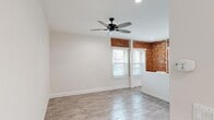 Located at 1057 S Western Ave in Los Angeles, this single-floor unit blends classic architectural character with fresh, modern finishes. The main living area makes an immediate impression with striking exposed red brick walls that wrap around multiple corners, creating a warm, industrial-chic aesthetic. Large windows fitted with white blinds allow natural light to fill the space, complementing the light-toned wood-look flooring that runs throughout. A sleek black ceiling fan with integrated lighting anchors the living area, enhancing both comfort and style. Recessed lighting adds a clean, contemporary touch to the ceilings. A low white partition wall defines the kitchen area, which is equipped with stainless steel appliances and benefits from abundant window light framed by the signature brick walls. The bedroom is a bright, neutral retreat with clean white walls, wood-look flooring, and access to a dedicated walk-in closet complete with built-in shelving. An additional storage space is also present. The bathroom features a full tub and shower combo with white tile surround, a vanity with cabinet storage, and wood-look flooring, maintaining the unit's consistent, clean aesthetic throughout.