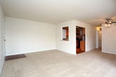 Located at 7701 Enfield Ave in Norfolk, Virginia, this single-floor residence offers a thoughtfully laid-out interior with distinct living, kitchen, and bedroom areas. The living space is generously sized, featuring plush wall-to-wall carpeting and large floor-to-ceiling sliding glass doors dressed with vertical blinds that allow abundant natural light and outdoor views. A ceiling fan adds both function and character to the open living area, which connects seamlessly to the kitchen via a pass-through window. The kitchen is well-equipped, showcasing warm honey-toned wood cabinetry, granite countertops, and a stylish mosaic tile backsplash. Black appliances, including a dishwasher, range, and refrigerator, complement the rich wood cabinetry, while light hardwood flooring adds warmth and continuity. The bedroom areas are carpeted and bright, each benefiting from large windows with vertical blinds that mirror the natural light found throughout the unit. One bedroom includes access to a closet, offering practical storage. A bathroom and additional utility areas complete the layout. The overall ambiance is clean, neutral, and move-in ready, with a cohesive design palette of warm beiges and whites that creates a welcoming and functional living environment.