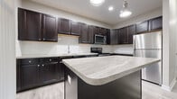 Located at 3400 Club Way Ct in Powell, Ohio, this 2-bedroom, 1-bathroom single-floor home offers a well-designed layout with modern finishes throughout. The open kitchen and living area serves as the heart of the home, showcasing rich dark cabinetry, light stone-toned countertops, a subway tile backsplash, a central island, and a full suite of stainless steel appliances including a refrigerator, range, microwave, and dishwasher. Recessed lighting and a pendant fixture illuminate the space, while light wood-look flooring flows seamlessly underfoot.

The living area features elevated ceilings with crown molding detail, neutral gray walls, and generous natural light. The primary bedroom is a well-proportioned retreat with plush carpeting and a walk-in closet with built-in wire shelving. The second bedroom offers large windows with outdoor views and matching wood-look flooring. The shared bathroom is finished with dark vanity cabinetry, a framed mirror, and coordinating light flooring. A dedicated laundry room accommodates a full-size washer and dryer with additional wire shelving above for storage. The home is completed by a closet and entrance area, providing practical organization from the moment you walk in.