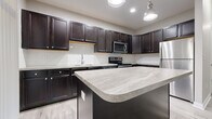 Located at 3400 Club Way Ct in Powell, Ohio, this 2-bedroom, 1-bathroom single-floor home offers a well-designed layout with modern finishes throughout. The open kitchen and living area serves as the heart of the home, showcasing rich dark cabinetry, light stone-toned countertops, a subway tile backsplash, a central island, and a full suite of stainless steel appliances including a refrigerator, range, microwave, and dishwasher. Recessed lighting and a pendant fixture illuminate the space, while light wood-look flooring flows seamlessly underfoot.

The living area features elevated ceilings with crown molding detail, neutral gray walls, and generous natural light. The primary bedroom is a well-proportioned retreat with plush carpeting and a walk-in closet with built-in wire shelving. The second bedroom offers large windows with outdoor views and matching wood-look flooring. The shared bathroom is finished with dark vanity cabinetry, a framed mirror, and coordinating light flooring. A dedicated laundry room accommodates a full-size washer and dryer with additional wire shelving above for storage. The home is completed by a closet and entrance area, providing practical organization from the moment you walk in.