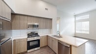 This three-bedroom, two-bathroom apartment in Placentia, California offers a well-designed single-story layout with contemporary finishes throughout. The kitchen is a standout feature, equipped with stainless steel appliances including a gas range, built-in microwave, dishwasher, and refrigerator. Light wood-toned cabinetry, a white subway tile backsplash, and light quartz countertops lend a clean, modern aesthetic, while a peninsula provides additional counter space and opens toward the living area, which benefits from natural light streaming through large windows. Hardwood-style flooring flows consistently throughout the unit, complementing the neutral, light-toned walls. Notably high ceilings amplify the sense of openness in the living room and bedrooms alike. The primary bedroom is a generous size and features a walk-in closet with wire shelving, offering ample storage. Additional bedrooms are well-proportioned with large windows that invite natural light and outdoor views. The bathrooms are finished with wood-toned vanities, quartz countertops, undermount sinks, and a shower-tub combination with white tile surround. Two hallways and two closets round out the floorplan, providing practical storage and ease of circulation throughout this thoughtfully appointed home.