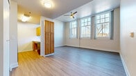 This single-floor, 1-bedroom, 1-bathroom unit offers a practical and well-designed layout making efficient use of its compact footprint. The combined kitchen and living room serves as the heart of the unit, featuring light wood-style luxury vinyl flooring, large multi-pane windows that flood the space with natural light, and a ceiling fan for year-round comfort. A standout feature is the pass-through window connecting the kitchen to the living area, creating an open and airy feel. The kitchen is equipped with warm wood-toned cabinetry, black appliances including a refrigerator and range, and a light stone-finish countertop. A full-height wooden storage cabinet provides additional organizational convenience near the kitchen entry. The bedroom is a comfortable, well-sized room featuring plush wall-to-wall carpeting, a closet with bifold doors, and a window with outdoor views. The bathroom is designed with accessibility in mind, featuring grab bars, wood-look vinyl flooring, and clean, neutral finishes. Throughout the unit, white walls and crisp baseboards contribute to a bright, clean aesthetic. The entryway is tidy and functional, offering a smooth transition into the main living space.
