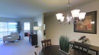 Located at 100 Fox Meadow Dr in Maple Shade, New Jersey, this single-floor residence offers a well-designed, open layout that connects living and dining areas seamlessly. The dining area is anchored by an elegant multi-arm chandelier with brushed nickel finish and frosted glass shades, casting warm, inviting light over a dark-toned dining table and chairs. Neutral-toned walls in soft green-gray hues complement the light carpeted flooring, creating a cohesive and calming aesthetic throughout the space. A dark credenza serves as a stylish accent piece, providing both storage and visual contrast against the lighter surroundings. The open sightlines extend into the living area and beyond, where natural light filters in through a window, enhancing the sense of openness and airiness. A mirrored surface in the background reflects additional light, further brightening the interior. The thoughtful flow between spaces makes the layout feel connected and functional. Overall, the residence presents a clean, modern ambiance with tasteful finishes and a comfortable, move-in-ready appeal suited for everyday living.