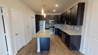 Located at 401S Coit Road in McKinney, Texas, this single-floor residence offers a well-designed layout with contemporary finishes throughout. The kitchen serves as the centerpiece of the home, showcasing rich dark cabinetry that extends to the ceiling, providing generous storage capacity. Granite countertops in a speckled neutral tone run across the perimeter surfaces and the central island, which also offers bar-style seating. A full suite of stainless steel appliances — including a refrigerator, range, and built-in microwave — complements the sleek aesthetic, while a subway tile backsplash adds a refined finishing touch. Pendant lighting hangs above the island, and recessed lighting illuminates the space efficiently. Wood-style plank flooring flows through the kitchen and open living area, lending warmth and visual continuity. The bathroom mirrors the kitchen's design language, featuring matching dark cabinetry, granite countertops, an undermount sink with chrome fixtures, and a framed vanity mirror. The bedroom is carpeted for comfort, with a window allowing natural light to filter in and a ceiling-mounted light fixture overhead. Throughout the residence, clean neutral wall tones and consistent trim work create a cohesive, move-in-ready environment.