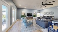 Located at 1900 54th Ave S in Saint Petersburg, Florida, this single-floor community space offers a thoughtfully designed layout that seamlessly blends comfort and modern style. Throughout, light wood-tone flooring, cool blue-gray walls, and recessed lighting create a cohesive, welcoming atmosphere.

The living room is generously proportioned, bathed in natural light streaming through large floor-to-ceiling windows and sliding glass doors that frame views of an outdoor pool area. A large ceiling fan anchors the vaulted ceiling, while comfortable seating, lush potted plants, and curated wall art contribute to a relaxed yet polished ambiance. A built-in workstation along one wall adds a practical touch, making the space versatile for both leisure and productivity.

The kitchen is equally impressive, featuring sleek dark cabinetry with brushed hardware, crisp white countertops, and stainless steel appliances including a large French door refrigerator. A spacious island with bar seating serves as a central gathering point, while a dedicated dining area with a round mirror accent rounds out the space. Skylights and overhead fixtures ensure bright, even illumination throughout. Together, these two areas form a cohesive, multifunctional space ideal for community gatherings.