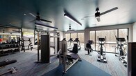 Located in Little Rock, Arkansas, this fitness center offers a thoughtfully designed exercise room that delivers a comprehensive workout environment. The space features a striking teal-painted ceiling accented by sleek linear lighting fixtures and ceiling fans, creating a modern, energetic ambiance throughout.

Large floor-to-ceiling windows line the perimeter, flooding the interior with natural light and offering views of the surrounding wooded landscape and exterior courtyard. The flooring blends patterned multi-tone carpet in the cardio zones with solid darker carpet in the strength training areas, providing both comfort and clear functional zones.

The cardio section is outfitted with multiple Spirit-brand treadmills, elliptical trainers, and a stair climber, each equipped with individual digital display consoles. A cable cross-training machine and a multi-functional strength station anchor the weight training area, which is further supported by a full dumbbell rack and an adjustable weight bench. Stability balls are neatly stored on a dedicated rack near the entrance.

Full-length mirrors along one wall enhance the sense of space and allow users to monitor their form. A wall-mounted flat-screen display adds an entertainment element. Double glass doors provide easy access, and the overall layout ensures ample circulation space between equipment, making this fitness center both functional and inviting.