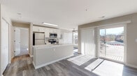 This single-floor residence offers a thoughtfully designed open-concept layout that seamlessly connects the kitchen and living areas. The kitchen is a standout feature, showcasing crisp white shaker cabinetry, striking marble-look quartz countertops, and a full suite of stainless steel appliances including a refrigerator, electric range, and over-the-range microwave. A peninsula with an integrated sink provides additional prep space and serves as a natural divider between the kitchen and the main living area. Durable wood-look luxury vinyl plank flooring runs throughout the main living spaces, complementing the neutral warm-toned walls and clean white trim. The living area is bathed in natural light, thanks to a sliding glass door that opens to a private balcony, offering outdoor views. A ceiling fan adds both style and function to this bright, airy space. The bedroom features plush wall-to-wall carpeting and a window that further enhances the sense of openness. The bathroom is well-appointed with a white vanity, tile flooring, a large mirror, and a tub-shower combination adorned with elegant marble-patterned tile surround. Ample closet storage is present throughout, and the unit includes an accessible electrical panel. The overall aesthetic is clean, contemporary, and move-in ready.