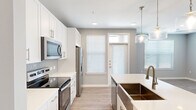 This single-story residence features a thoughtful layout across a comfortable footprint, designed with modern finishes and functional living spaces. The open-concept kitchen serves as a central highlight, featuring white shaker cabinetry, a subway tile backsplash, stainless steel appliances including a range, microwave, and refrigerator, and a large island with a white quartz countertop and an undermount bronze-toned sink. Glass pendant lights hang above the island, adding a contemporary touch, while light wood-style flooring extends throughout the main living areas.

The living room connects seamlessly to the kitchen, benefiting from natural light through sizable windows with white blinds. Both bedrooms are carpeted and include ceiling fans and dedicated closets. The generously sized primary bedroom features multiple windows and a walk-in closet with built-in shelving and hanging rods. The second bedroom also includes its own walk-in closet with similar storage configurations.

Each bathroom is finished with white vanities, tile surround tub-shower combinations, and brushed nickel fixtures. A dedicated laundry room houses a full-size washer and dryer with overhead shelving. The overall palette of soft grays, white trim, and warm wood-tone flooring gives the residence a clean, cohesive, and contemporary aesthetic.